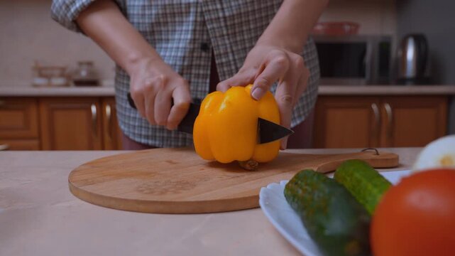 Vegetables are cooked. Preparing salad ingredients by hand by slicing and slicing. Close-up of slicing yellow bell peppers on a wooden board in the kitchen