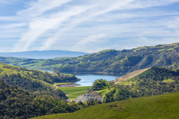 Serene landscape of rolling green east bay hills surrounding a calm San Antonio Reservoir. Sunol Wilderness, Alameda County, California.