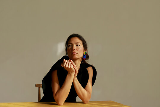 Woman Sitting at Table With Hands Clasped in Bright Room