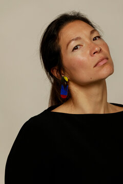 Woman Poses With Colorful Earrings Against a Simple Background