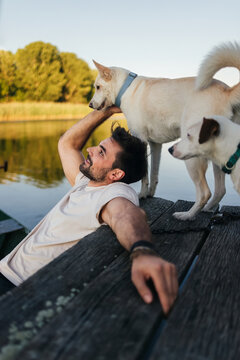 Man Relaxing With Dogs On Dock By Water
