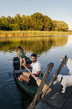 Friends Rowing Boat on Calm River with Dock and Dogs