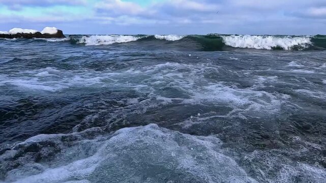 Black Sea: waves wash over natural coquina limestone stones covered with a layer of green algae along the shoreline of a beach in Odessa, Ukraine