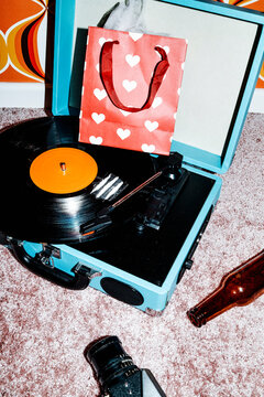 a vinyl with cocaine lines on a player beside a heart paper gift bag