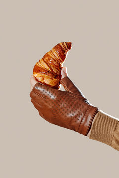 a man holds a croissant wearing a brown leather glove