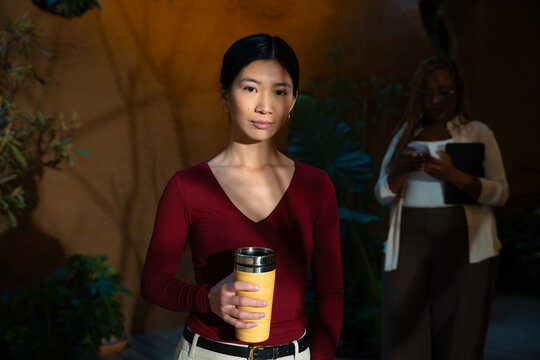 Professional asian woman holding coffee in office garden