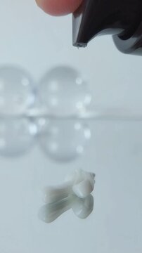 Pouring skin cream onto a reflective glass surface, close up view, cream texture, skincare product presentation, cosmetic concept with mirror effect.