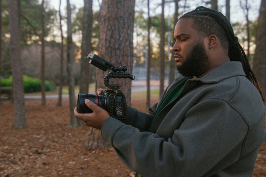 Videographer Holds Camera While Standing in Wooded Area During Sunset