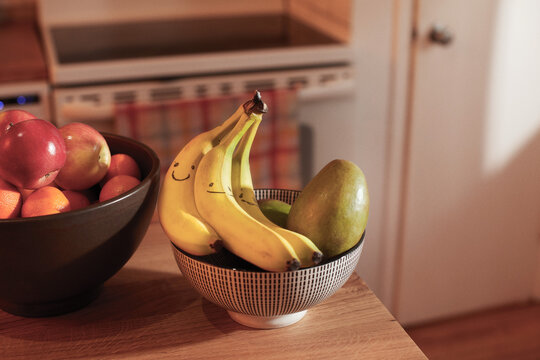 Bananas with Smiley Faces in Fruit Bowl on Kitchen Counter