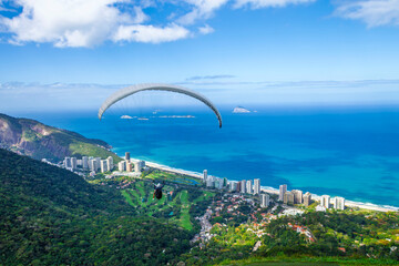 Paraglider soaring over the Atlantic Ocean and São Conrado beach with a view of the green mountains and luxury buildings in Rio de Janeiro, Brazil. © lcrribeiro33@gmail