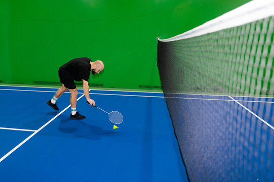 Person Plays Badminton on a Blue Court With a Green Background