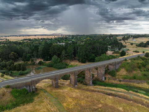 Rain falling from a dark sky over an arched railway viaduct and valley