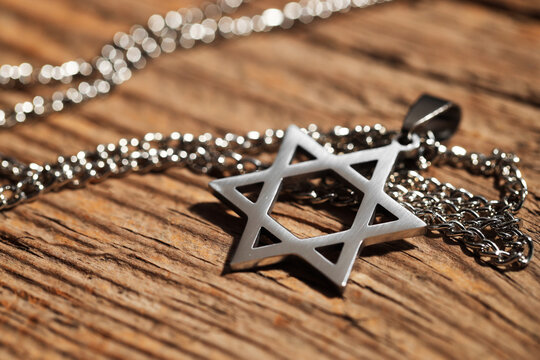 Holocaust Remembrance Day. Pendant in shape of Star of David and metal chain on wooden table, closeup