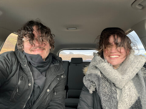 Man and woman smiling and taking a selfie with windblown hair 