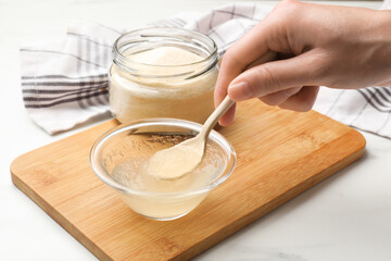 Woman stirring bloomed gelatin with spoon at white table, closeup