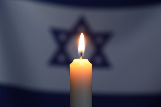 Holocaust Remembrance Day. Burning candle against flag of Israel, closeup