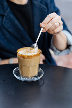 Person stirring foamy latte in glass cup