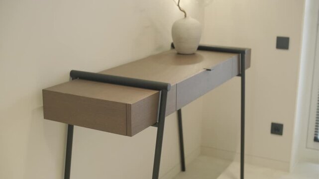 Modern minimalist console table with decorative vase and glass wall sconce.