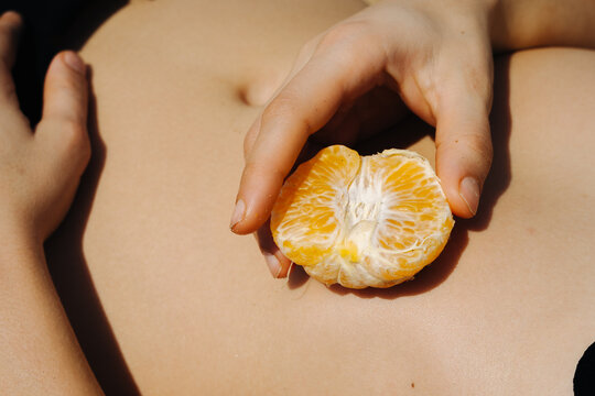 Hands Hold a Fresh Orange Segment on Skin in Sunlight