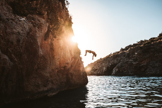 boy jumping from cliff into sea at sunset in greece