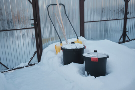 Snow covers black bins and sled in a storage area during winter
