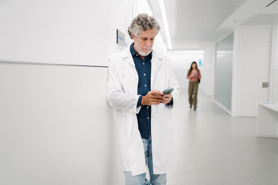 Senior doctor using smartphone in hospital corridor