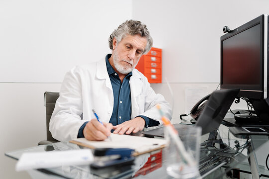 Senior doctor writing medical notes in office