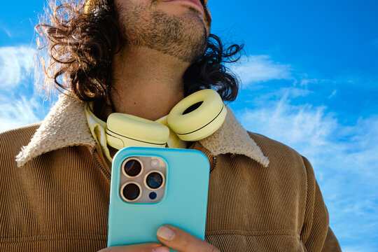 Man Holding Smartphone with Headphones Around Neck