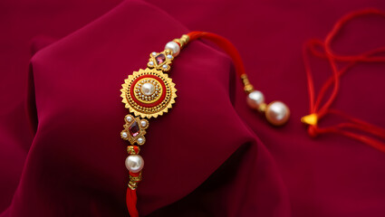 An exquisite golden and pearl studded Rakhi bracelet rests elegantly on a rich maroon fabric.