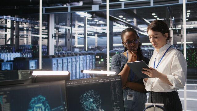 Teamworking engineers in data center integrate AI automation tools together during maintenance session. Server room colleagues configure machine learning models across server infrastructure, camera A