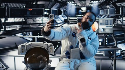 Fototapeta premium Astronaut taking selfie pictures with smartphone, making hand gestures during planet colonization mission. Orbit station crew member doing photographs with mobile phone during cosmic journey