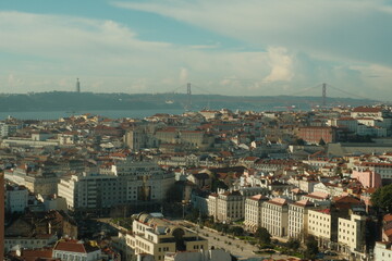 Naklejka premium Beautiful red roof tops of portuguese buildings in lisbon on a sunny day with blue sky with ponte 25 abril bridge in back