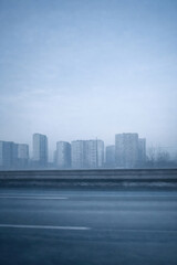 Fototapeta premium A foggy cityscape with silhouettes of multi-story residential buildings against a cold blue sky. 