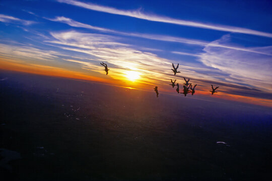 Skydiving formation flying upside down at sunset, captured on slide film in the early 2000s. Silhouetted parachutists against dramatic orange horizon and deep blue sky.