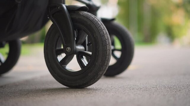 Stroller wheel closeup rolling on asphalt pavement, black rubber tire with deep tread, smooth rotation and reliable suspension, blurred park background, active commute vibe, durable design for family