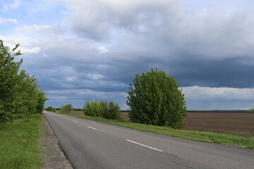 Country road beside agricultural field under dramatic cloudy sky