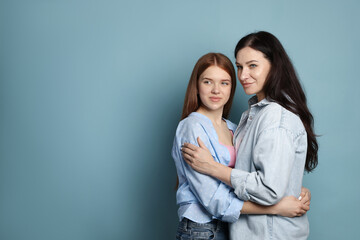 Fototapeta premium Mother and her teenage daughter hugging on light blue background. Space for text
