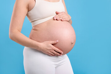 Pregnant woman touching her belly on light blue background, closeup