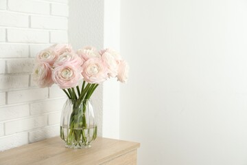 Fototapeta premium Beautiful ranunculus flowers in glass vase on wooden chest of drawers near white wall indoors. Space for text