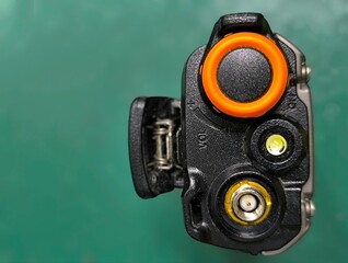 A high-angle, close-up shot of a black handheld radio transceiver (walkie-talkie). The image focuses on the top control panel featuring an orange power/volume dial, an LED indicator light, and a gold-