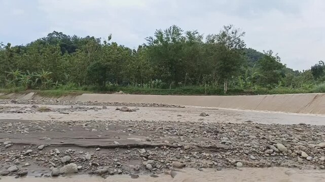 Video of water flowing over a small dam or river overflow structure with surrounding green landscape. Natural outdoor scene showing water movement, irrigation system, and environmental concept. Suitab