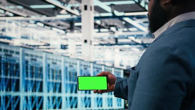 Green screen smartphone used by server farm worker to optimize electronics. Data center admin using chroma key phone to monitor system performance and fix bottlenecks, camera A