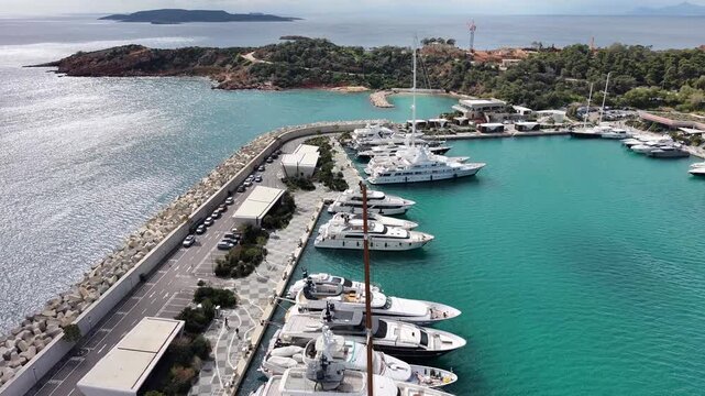 Aerial view of Vouliagmeni Nautical Club marina near Temple of Apollo Zoster with luxury yachts docked in turquoise waters, parking area and rocky coastline, Greece