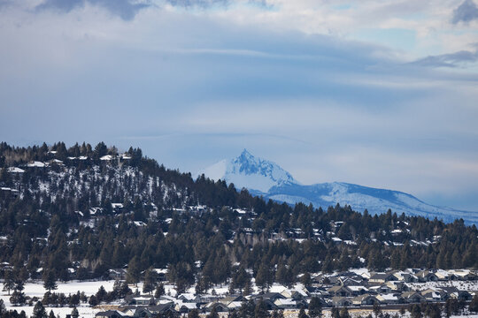 A mountain range with snow on it and houses in the valley below. The sky is cloudy and the mountain is visible in the distance