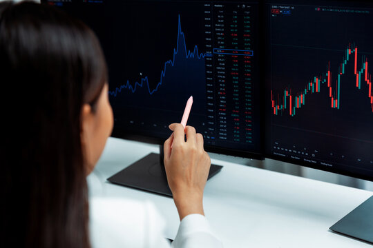 Young beautiful Asian businesswoman pointing with pen in exchange stock market on pc screen at back side view, analyzing profit at modern office, investing high profit valed in wealth. Stratagem.
