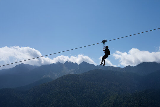Person zipline mountain, Dolomites green forest, bright blue sky white clouds, adventure tourism adrenaline experience extreme sport freedom