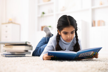 Fototapeta premium Cute little girl reading book on floor at home