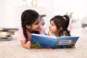 Fototapeta premium Cute little girls reading book together at home