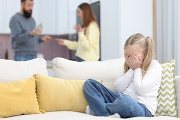 Obraz premium Alimony. Sad little girl sitting on sofa while her parents arguing at home, selective focus