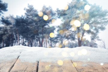 Fototapeta premium Wooden surface covered with snow against forest in winter, bokeh lights